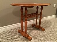 Full view of the oval maple end table showing side profile with turned legs and horizontal supports, standing on carpeted floor.