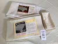 Three vintage sheer tablecloths with floral patterns and original labels displayed folded and stacked with matching napkins.