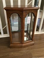 Front view of small wooden curio cabinet showing glass double doors and wood grain finish.