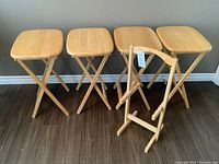 Front view of four wooden snack tables with folding legs and the wooden stand.