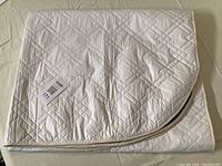 Folded quilted table pad showing white top side with diamond pattern stitching and partial brown underside.