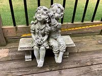 Two-piece resin child statue seated on bench with measuring tape showing height and length.