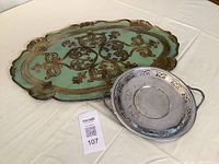 Two trays on white tablecloth: large ornate Italian tray with turquoise and gold design and smaller round Canadian silverplate tray with handles