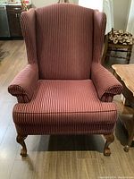 Front view of the red and beige striped wing chair showing upholstery and wooden legs.