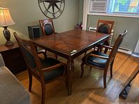 Four matching wood frame dining chairs around a wooden dining table, black faux leather upholstery on seat and back