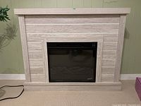 Front view of electric fireplace with faux wood laminate mantel against green wall and beige carpet