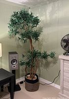 Full view of the artificial indoor plant with multiple dried wood branches and green leaf clusters in woven basket planter.