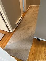 Full view of beige polyester carpet runner in hallway on hardwood floor showing length and wall proximity