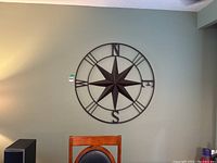 Metal compass wall art mounted on wall above chair, showing full 39x39 inch size.