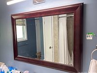 Front view of large rectangular mirror with beveled edges in a composite wood frame with reddish-brown finish hanging on a bathroom wall.