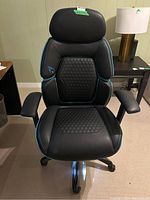 Front view of black leather office chair with hexagonal quilted seat and back with blue contrast trim and padded armrests.