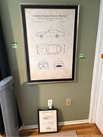 Two framed patent prints displayed—one larger on wall, one smaller on floor leaning.