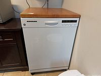 Frontal view of a GE portable dishwasher with white front and wood-effect top panel, showing control buttons and vent on the front.