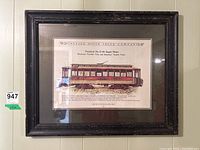 Framed railway print inside a dark brown/black antiqued wooden frame with slight wear. The illustration shows a vintage railway car and includes technical descriptive text.