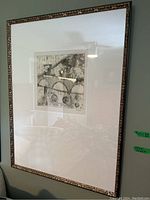 Full view of the framed wall art hung on a wall showing the ornate frame and white matting.