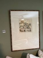 Framed paper and metallic wall art with tan mat and textured metallic bronze composite frame on green wall above couch.