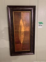 Rectangular abstract foliage wall art piece featuring a stylized single leaf in warm earthy tones, framed with composite dark brown and gold accents.