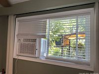 White PVC horizontal window blinds installed in window with air conditioning unit.