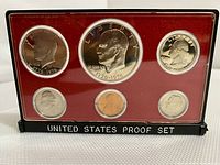 Front view of the 1975 S US Proof Bicentennial Coin Set in plastic case. Shows six coins with clear Bicentennial designs against a red backdrop in black casing.