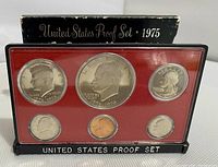 Front view of coins in original plastic red felt holder with black base labeling and worn black outer box.