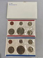 Two 1976 US Mint Bicentennial Uncirculated Coin Sets in sealed cellophane packaging. Coins include penny, nickel, dime, quarter, half dollar, and dollar with Bicentennial designs. Packaging shows wear from age.
