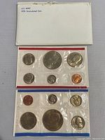 Two uncirculated sets of 1976 US Bicentennial coins encased in cellophane, placed beneath original white envelopes with visible wear.