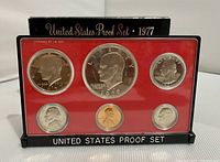 Front view of 1977 US proof coin set showing six coins in red plastic insert with black plastic frame and base.