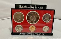 Full front view of 1977 US Proof Coin Set in plastic case with red insert featuring six coins including Lincoln cent, Jefferson nickel, Roosevelt dime, Washington quarter, Kennedy half dollar, and Eisenhower dollar. Black exterior case behind set labeled 'United States Proof Set - 1977'.