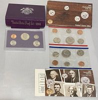 Top view showing all coin sets including purple proof set case, wooden card uncirculated set, two cellophane sealed mint sets, and informational pamphlets