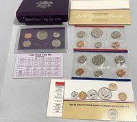 Overview of all included coin sets including proof set in plastic case, two uncirculated mint sets in cellophane, and informational pamphlets.