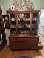 Full front view of the wooden Knechtel dining room cabinet with glass upper doors showing shelves and various decorative items inside.