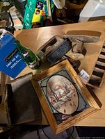 Photo of lot showing antique iron, green glass bottle, first aid kit box, cast iron item, wooden pulley, framed mirrored painting, and wooden tray.