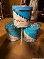 Three vintage Player's cigarette tobacco tins stacked in a pyramid, showing tops and sides with brand and health warning label.