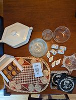 Photo showing assorted vintage serving items including white ironstone lidded dish, wicker placemats, ceramic bird salt and pepper shakers, black and white coasters, various glass bowls and plates.