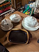 Photo showing three white Wedgwood lidded dishes on a table along with one rectangular brown and black Butters London baking dish.