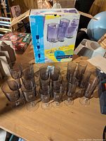 Eighteen Luminarc purple-tinted glasses arranged in groups on a wood surface with original blue and yellow Luminarc box behind them.