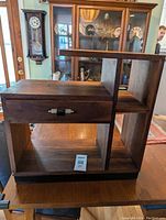Mini Art Deco shelving unit made of dark wood with a drawer and multiple open shelves, shown from a slightly angled front view to reveal construction and drawer placement