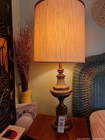 Single brass Mid-century Modern Stiffel lamp on wooden side table with beige lampshade illuminated.