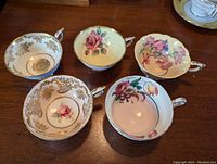 Top view showing floral and gold designs inside five Paragon tea cups arranged on a wooden surface.