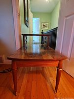 Side view of two sets of two-tiered wood tables showing wood grain surface and tapered legs with some gold rings on legs.