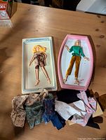 Two vintage flip and fold paper dolls styled like Barbie on trays with assorted paper doll clothing