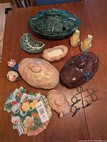 Overview of various vintage ceramic vegetable dishes including cabbage and potato shapes, salt and pepper shakers, and napkin rings on a wood table.
