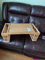 Wicker laptop/breakfast tray resting on a dark leather couch to show overall shape and size, including handles and legs raising the tray surface.