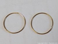 Pair of gold hoop earrings side by side on a plain white surface, showing full round shape and smooth polished finish.