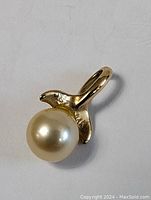 Front view of 14K gold whale tail pendant holding a pearl, showing shape and luster.