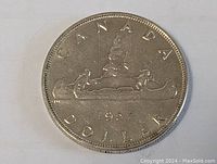 Full reverse side of the 1957 Canada silver dollar coin showing the canoe and denomination.