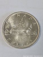 Obverse side of the 1965 Canadian silver dollar coin showing the canoe design with two people and the year 1965.