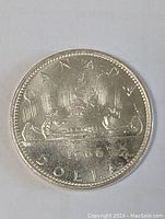 Photo of the reverse side of the 1966 Canadian silver dollar coin showing the canoe design with two men paddling and the inscriptions.