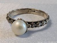 Front and angled views of antique sterling silver ring with large pearl set center and oxidized floral pattern band.