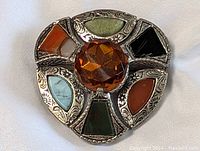 Front close-up image of large vintage multi-colored stone pin brooch with ornate silver-tone metal setting and faceted amber center stone.